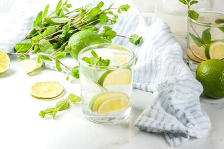 Homemade lemonade or mojito cocktail with fresh lime and mint leaves, white marble background, copy...