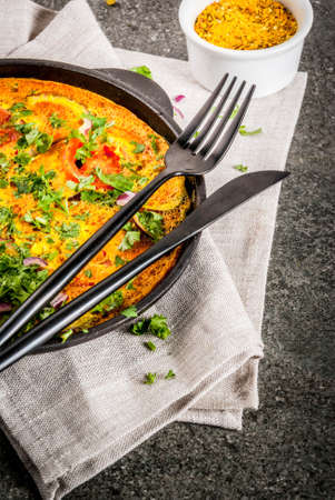 Indian food recipes, Masala Omelette with fresh vegetables - tomato, hot chili pepper, parsley, dark stone background, copy spaceの写真素材
