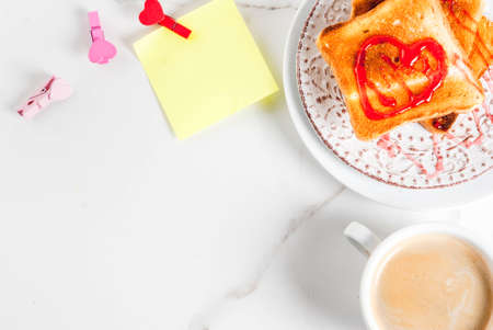 Valentine's day breakfast idea with coffee mug, toasted bread with red strawberry jam, blank paper note for congratulations with heart shaped pins, white marble background, copy space top viewの写真素材