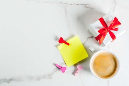 Valentine's day concept, gift box with red ribbon, coffee mug, blank paper note for congratulations with heart shaped pins, black background, copy space top viewの写真素材