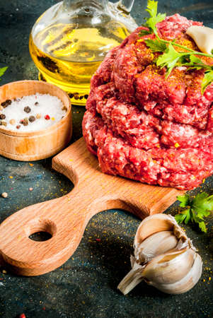 Raw burger cutlets with salt, pepper, oil, herbs and spice, on dark table, copy spaceの写真素材