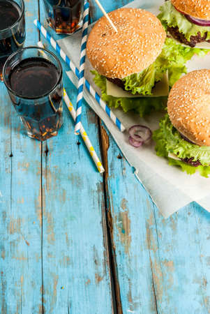 Picnic, Fast food. Unhealthy food. Delicious Fresh Tasty Burgers with Beef Cutlet, fresh Vegetables and Cheese on old rustic blue wooden table with sweet soda water. Copy space top viewの写真素材