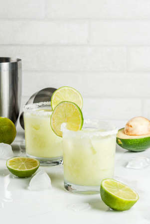 Alcoholic cocktail recipes and ideas. Avocado and lime margarita with salt, on a white marble kitchen table. Copy spaceの写真素材