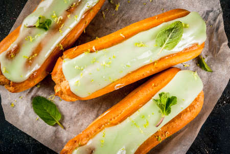 Traditional French dessert. Mojito Eclairs with lime zest and mint leaves, on dark blue background,...