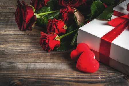 Holiday  background, Valentine's day. Bouquet of red roses, tie with a red ribbon, with wrapped gift box. On wooden table, copy spaceの写真素材