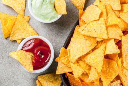 Tasty mexican snack,  tortilla chips nachos with ketchup and guacamole, grey stone table, copy space...