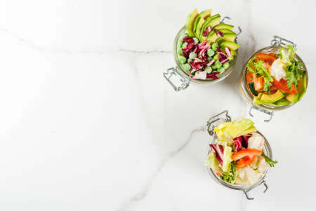 Fresh salads in jar with fresh vegetables and healthy dressings,  on white marble table, copy space