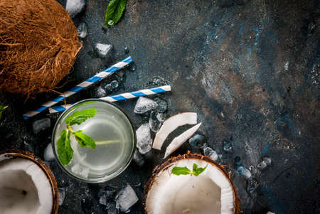 Healthy food concept.  Fresh Organic Coconut Water with coconuts, ice cubes and mint, on rusty dark blue background, copy space top viewの写真素材