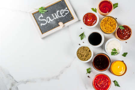 Set of different sauces - ketchup, mayonnaise, barbecue, soy, teriyaki, mustard, grain hills, pesto, adzhika, chutney, tkemali, pomegranate sauce on white marble background. Top view copy spaceの写真素材