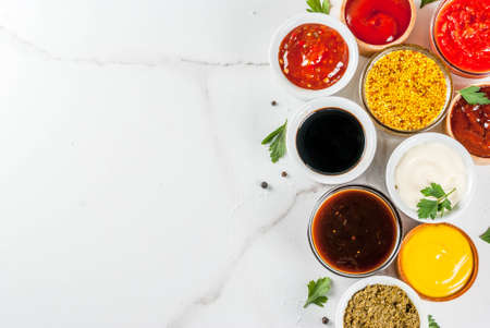 Set of different sauces - ketchup, mayonnaise, barbecue, soy, teriyaki, mustard, grain hills, pesto, adzhika, chutney, tkemali, pomegranate sauce on white marble background. Top view copy space