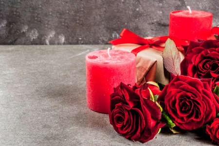Holiday  background, Valentine's day. Bouquet of red roses, tie with a red ribbon, with wrapped gift box and red candle. On a gray stone table, copy spaceの写真素材