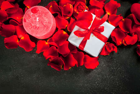 Valentine's day concept, with rose flower petals and white wrapped gift box with red ribbon, on dark stone background, copy space top viewの写真素材