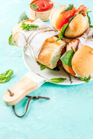 Fresh baguette sandwich with bacon, cheese, tomatoes and spinach, light blue background copy spaceの写真素材
