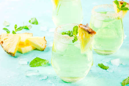 Tropical drink, Pineapple juice margarita cocktail with fresh mint, light blue background copy space
