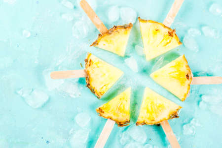 Slice pineapple popsicle sticks and mint leaves, on light blue background with ice, summer concept,...
