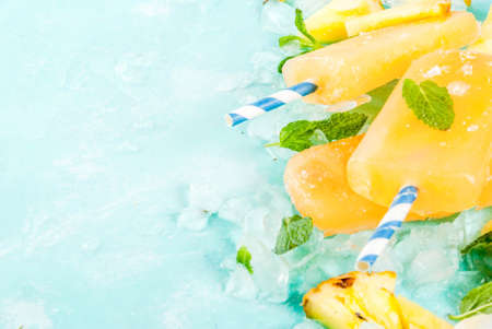 Homemade Pineapple Popsicles on Ice with fresh Pineapple slices and mint, on light blue background copy spaceの写真素材