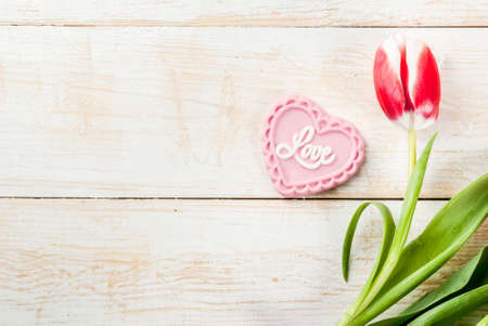Valentines day background for congratulations, greeting cards. Fresh spring tulips flowers with pink chocolate candy, on white wooden background top view copy spaceの写真素材