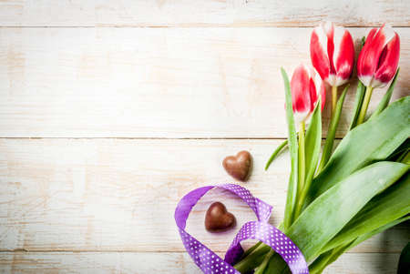 Valentines day background for congratulations, greeting cards. Fresh spring tulips flowers with chocolate hearts candy, on white wooden background top view copy spaceの写真素材