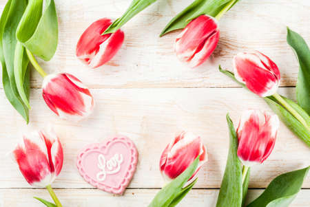 Valentines day background for congratulations, greeting cards. Fresh spring tulips flowers with pink chocolate candy, on white wooden background top view copy space frameの写真素材