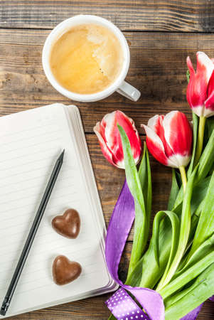 Valentines day background for congratulations, greeting cards. Fresh spring tulips flowers with notepad, chocolate hearts candy and coffee mug, on a wooden background top view copy spaceの写真素材