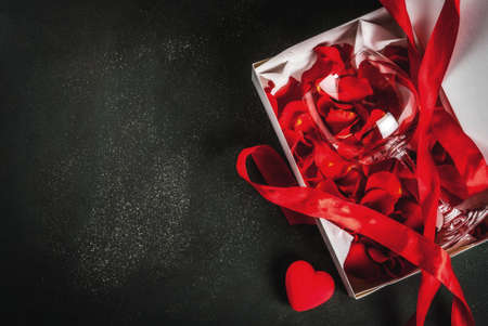 Valentine's day concept, white wrapped gift box with red ribbon, with rose flower petals in wine...