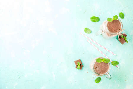 Chocolate smoothie or milkshake with mint and straw, in mason jar on light blue background, copy...
