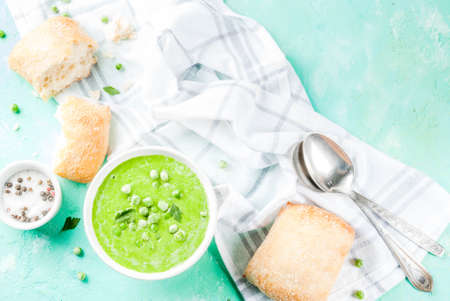 Green pea soup with fresh bread on light blue concrete table, copy space top viewの写真素材