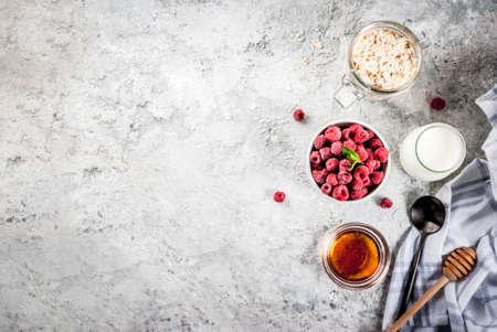Raw ingredients for summer healthy breakfast, cereals (oats), fresh Raspberry, mint leaves, yoghurt, honey, on light concrete background, top view, copy spaceの写真素材