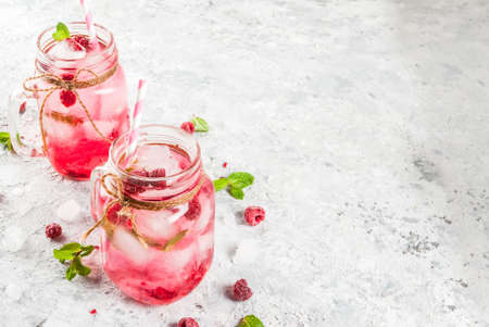 Cold summer drink, Raspberry Sangria, Lemonade or Mojito with fresh Raspberry and syrup, mint leaves, on grey stone background copy spaceの写真素材