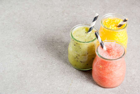 Detox organic diet drinks, homemade tropical smoothies - kiwi, orange, grapefruit, in portioned jars, on a gray stone table. Copy spaceの写真素材