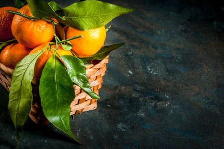 Fresh raw organic Tangerines with green leaves in little basket on dark concrete stone background, copy spaceの写真素材