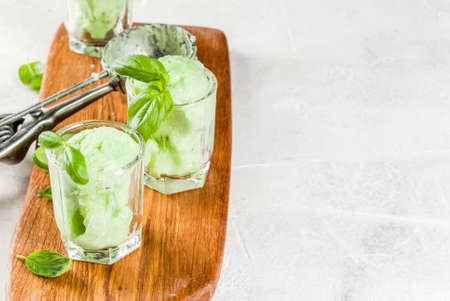 Summer desserts. Vegan food. Basil ice cream in serving glasses, decorated with fresh basil leaves. On a wooden cutting board, on a stone white table. Copy spaceの写真素材