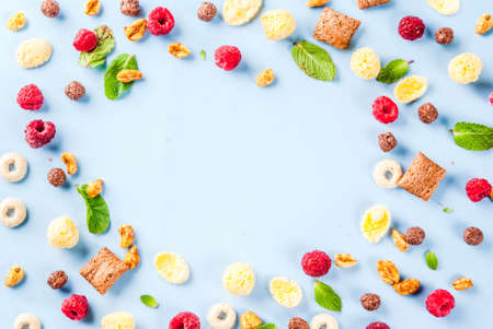 Healthy breakfast ingredients concept. Various breakfast cereal, raspberries and mint on blue background, copy space top view frameの写真素材
