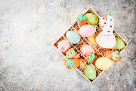 Easter holiday concept, sweet cookies in form of carrots, Easter bunny, with colorful eggs, top view, grey stone background copy spaceの写真素材