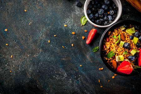 Healthy breakfast with muesli or granola with nuts and fresh berries and fruits - strawberry, blueberry, kiwi, on dark blue table, copy space top viewの写真素材