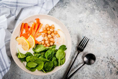 Modern vegan food, savory yogurt bowl with beans, chickpeas, spinach, spicy carrots, lemon, Gray stone background, copy space top viewの写真素材