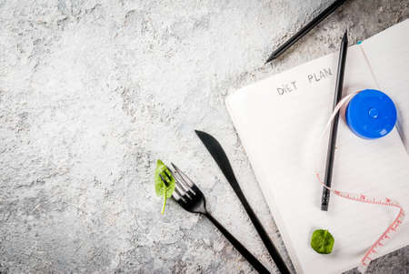 Diet plan weight lose concept, fresh vegetable salad with fork, knife, note pad,  grey stone table copy space top viewの写真素材