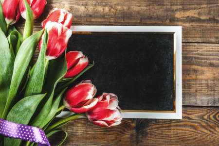 Background for congratulations, greeting cards. Fresh spring tulips flowers with chalkboard for text, on a wooden background top view copy spaceの写真素材