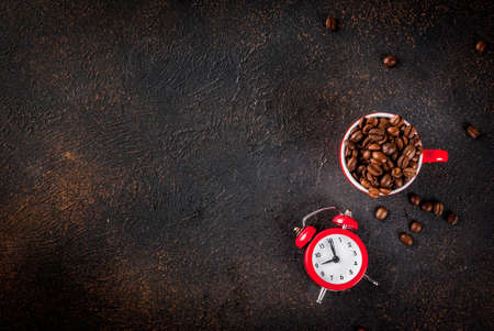Concept of a cheerful, good start to the day, morning coffee. Dark rusty background with coffee beans, an alarm clock and a cup of coffee. Top view copy spaceの写真素材