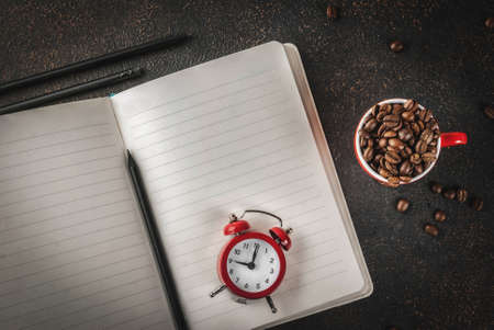 Concept of a cheerful, good start to the work day, morning coffee. Dark rusty background with coffee beans, alarm clock, notepad and a cup of coffee. Top view copy spaceの写真素材