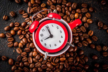 Concept of a cheerful, good start to the day, morning coffee. Dark rusty background with coffee beans, an alarm clock and a cup of coffee. Top view copy spaceの写真素材