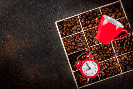 Concept of a cheerful, good start to the day, morning coffee. Dark rusty background with coffee beans, an alarm clock and a cup of coffee. Top view copy spaceの写真素材