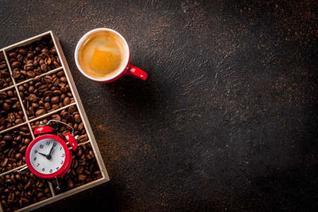 Concept of a cheerful, good start to the day, morning coffee. Dark rusty background with coffee beans, an alarm clock and a cup of coffee. Top view copy spaceの写真素材