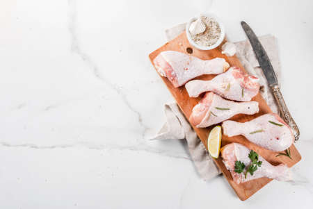 Raw meat, chicken legs, with olive oil, herbs and spices, on white marble background, copy space top viewの写真素材