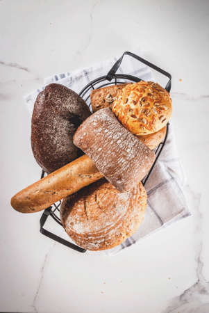 Variety of fresh homemade grain bread, in a metal basket, white marble background copy space top viewの写真素材