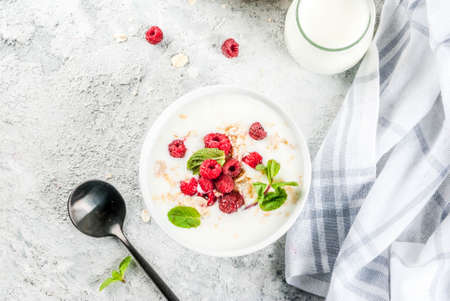 Raw ingredients for summer healthy breakfast, cereals (oats), fresh Raspberry, mint leaves, yoghurt,...