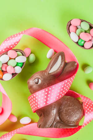 Easter holiday greeting card background, with chocolate easter bunny, candy eggs, quail eggs and festive ribbon, copy space top viewの写真素材