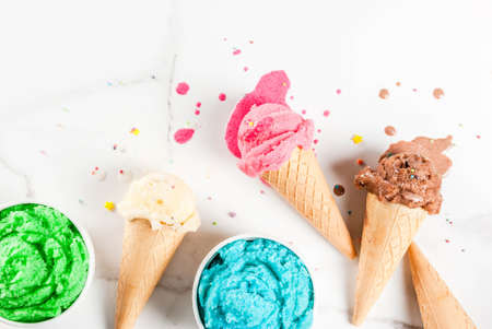 Different homemade melting ice cream in bowls and waffle ice cream cones, white vanilla, orange, pink berry, green, blue, chocolate white marble background  copy space top viewの写真素材