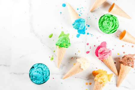 Different homemade melting ice cream in bowls and waffle ice cream cones, white vanilla, orange, pink berry, green, blue, chocolate white marble background  copy space top viewの写真素材
