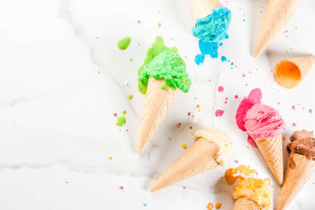 Different homemade melting ice cream in bowls and waffle ice cream cones, white vanilla, orange, pink berry, green, blue, chocolate white marble background  copy space top viewの写真素材